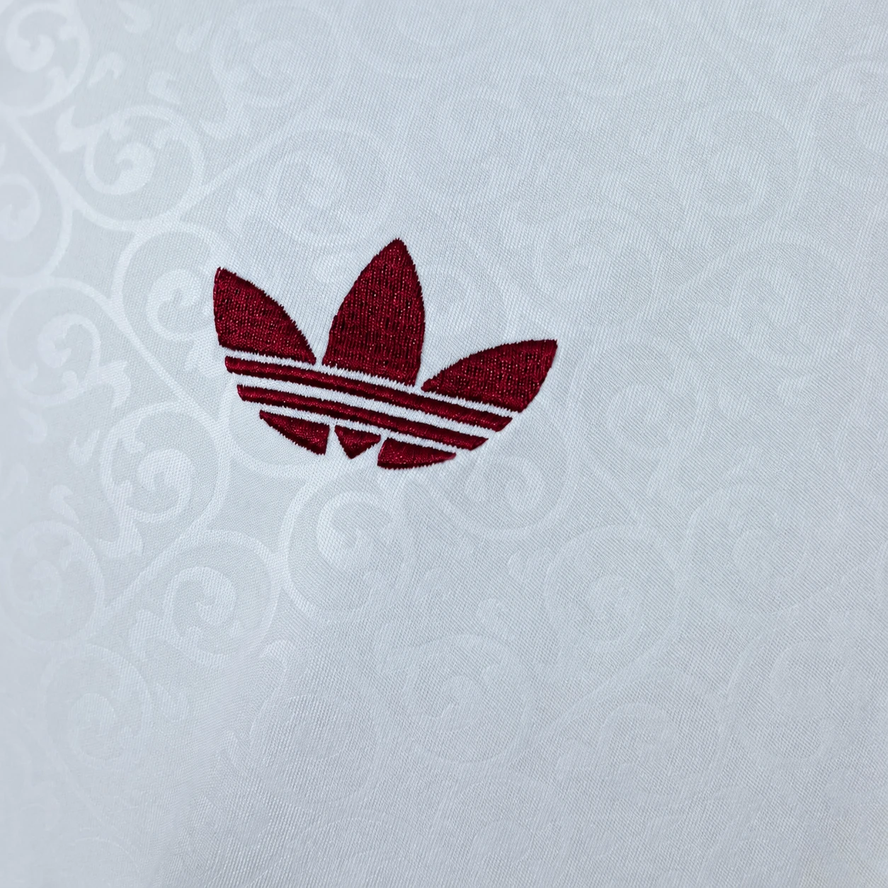 Close-up of a burgundy embroidered brand mark on patterned white jersey fabric