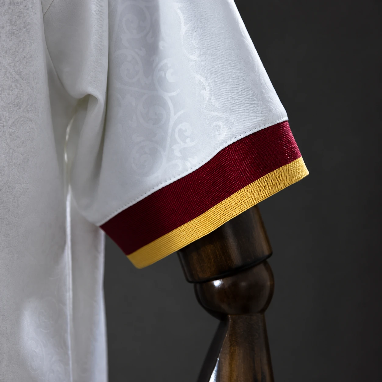 Close-up of a white football jersey sleeve with burgundy and gold cuff finish